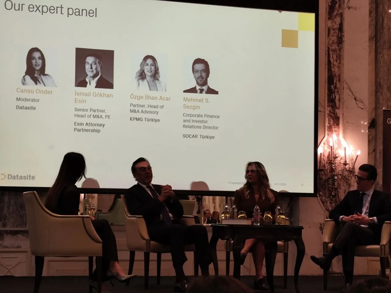Datasite Dealmakers Dialogues sempozyumunda sahnedeki uzman paneli; arkadaki ekranda konuşmacılar Cansu Önder, İsmail Gökhan Esin, Özge İlhan Acar ve Mehmet S. Sezgin'in adları yer alıyor